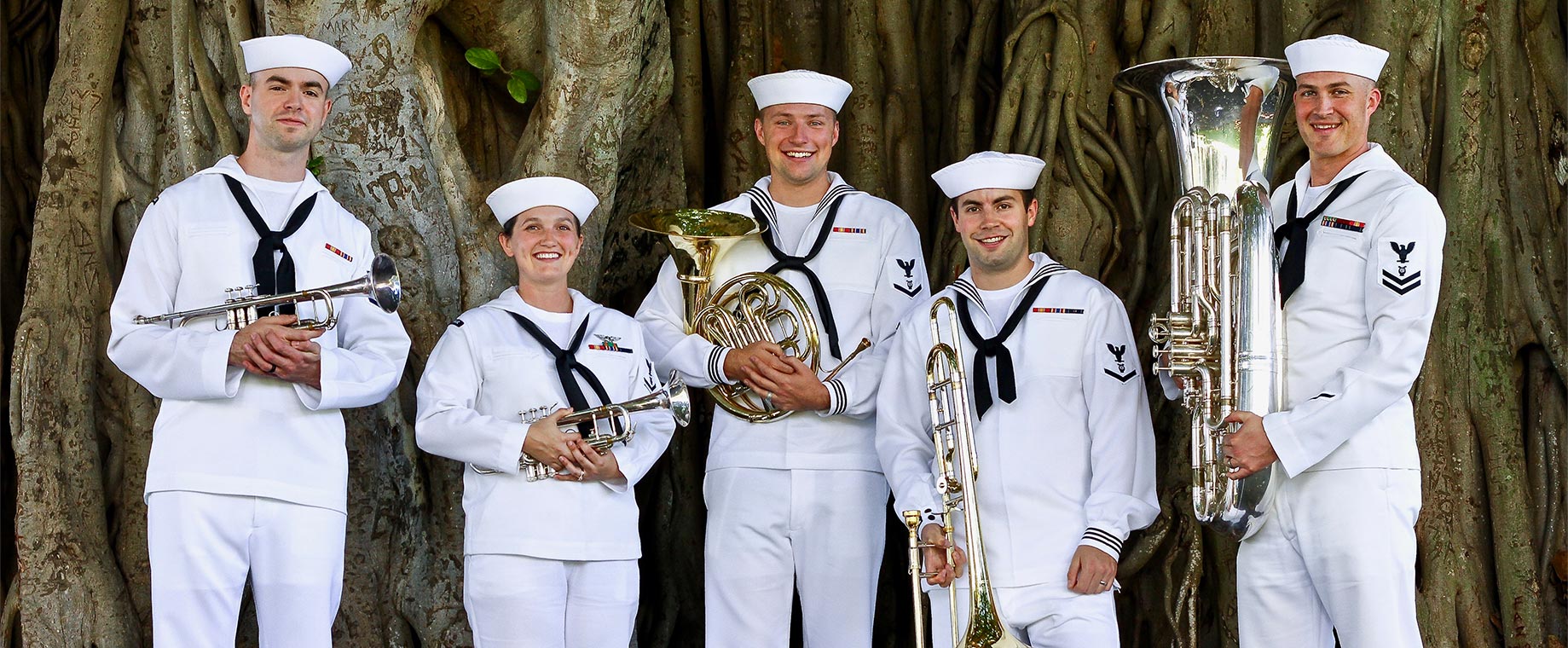 Five Sailors smile for the camera while holding musical instruments: two trumpets, a french horn, a trombone and a tuba.